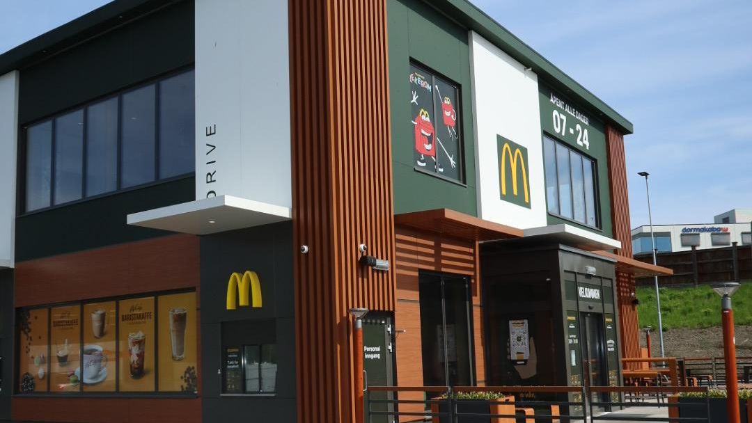 Moderne McDonald’s-restaurant med trepanel, store vinduer og skilt for åpningstider.